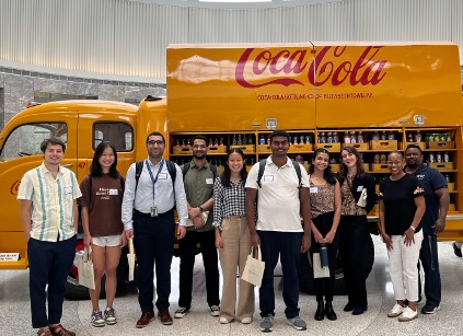 Group of students stand in front of a vintage yellow Coca-Cola delivery truck following a tour of the company's headquarters