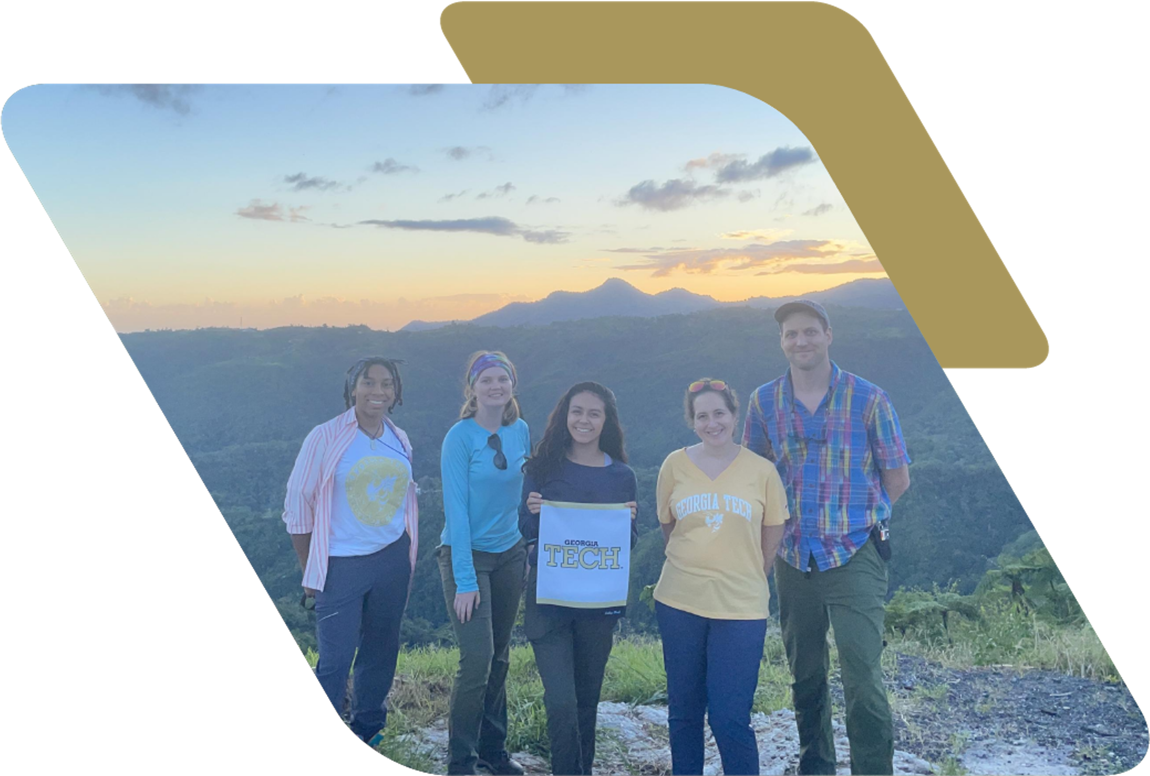A group of five people standing on a mountain overlook during sunset. One of the individuals is holding a small white banner that says Georgia Tech.