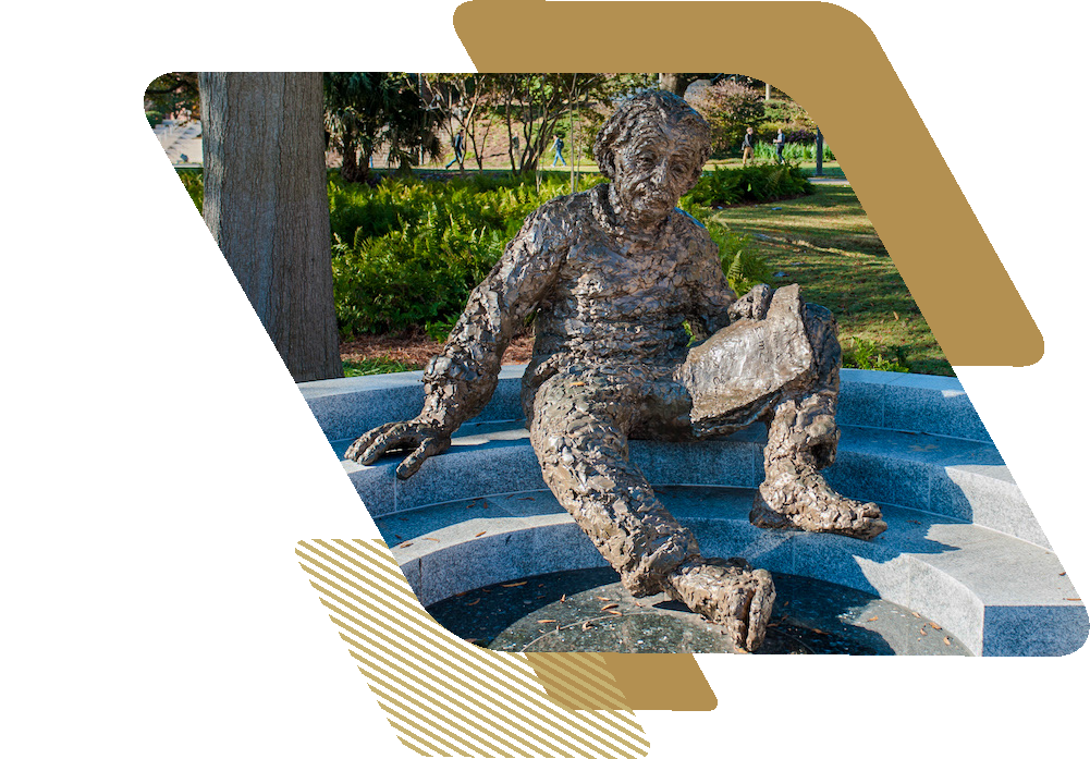 A larger-than-life bronze statue of Albert Einstein sitting with a notebook.