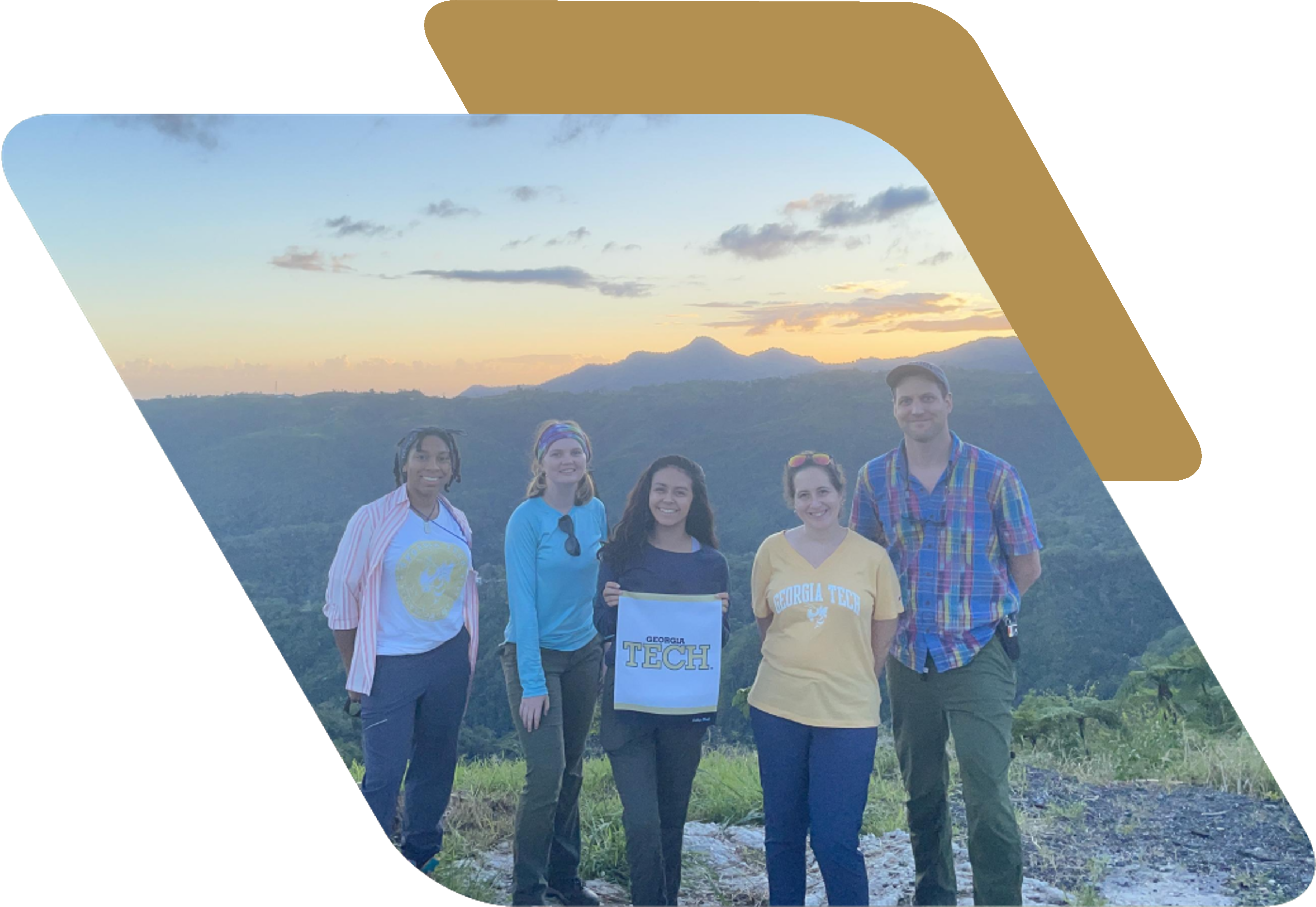 A group of five people standing on a mountain overlook during sunset. One of the individuals is holding a small white banner that says Georgia Tech.