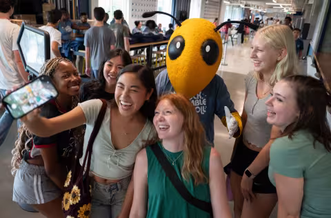 students taking a photo selfie with mascot Buzz.