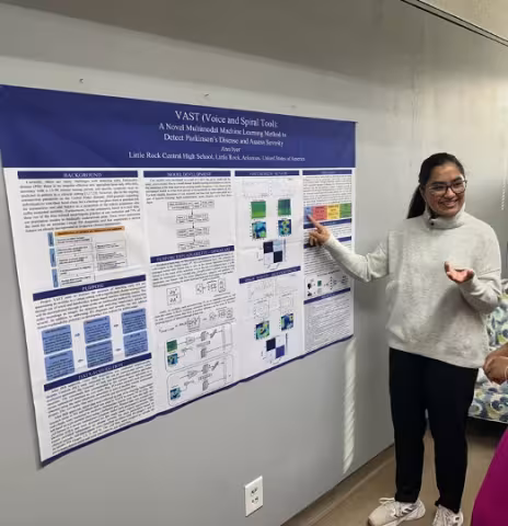 Young woman standing in front of a poster describing her Parkinson's Disease research
